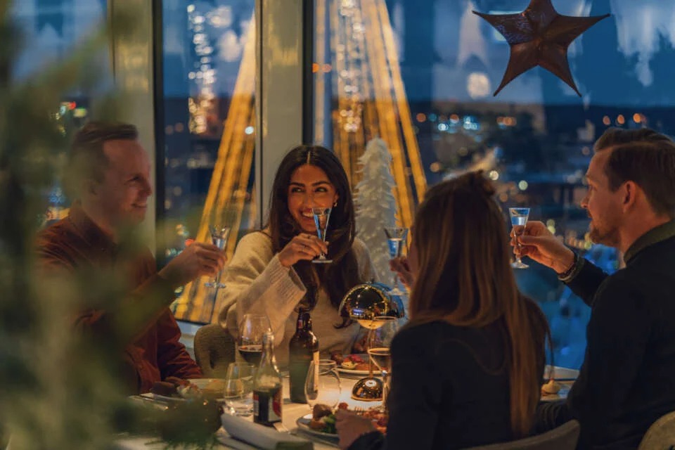 Four people raising a toast at a Christmas-decorated dinner table overlooking Gothenburg.
